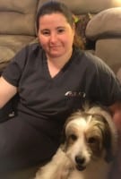 A person in dark scrubs sits on a couch with a white and brown dog resting beside them, both looking toward the camera.