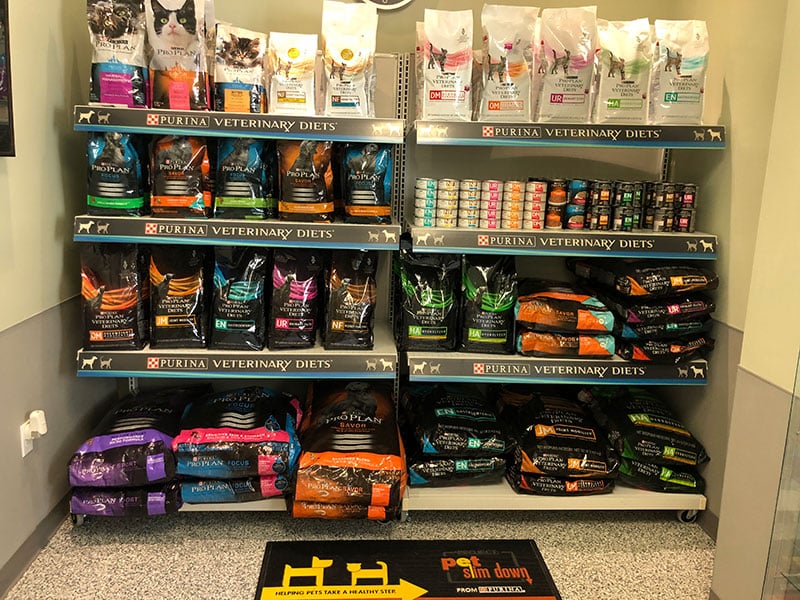 Shelves display various bags and cans of Purina Veterinary Diets pet food, including both dry and wet food options for cats and dogs, organized by brand and type.