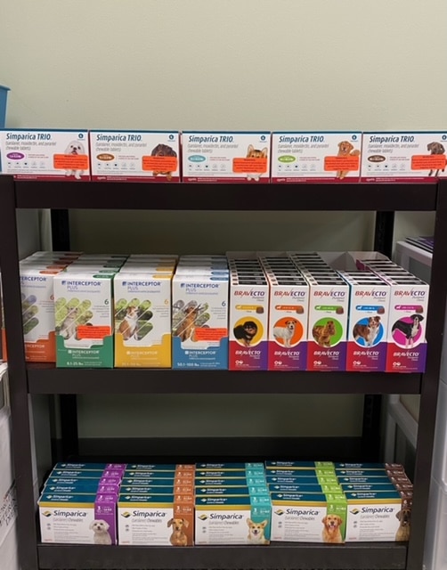 Shelves stocked with various boxes of pet medications, including Simparica TRIO, Interceptor Plus, and Bravecto, organized by brand and type.