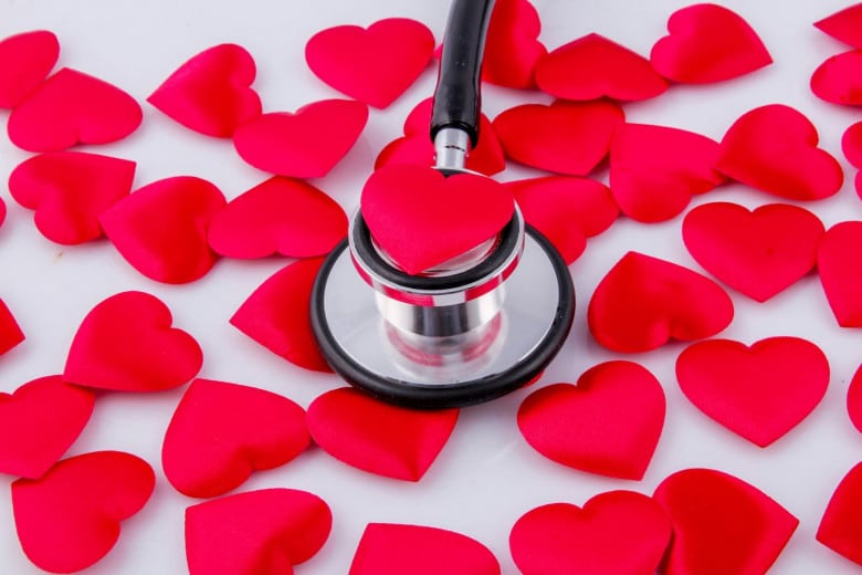A stethoscope placed on a red heart-shaped object, surrounded by many similar red heart shapes scattered on a white surface.